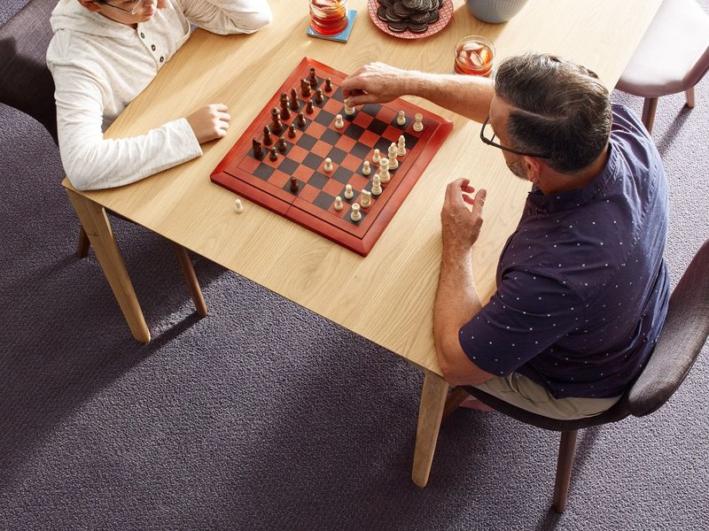 father and son playing chess while eating snacks in a room with gray carpet from Richardson’s Carpet Service in the Williamsburg, VA area
