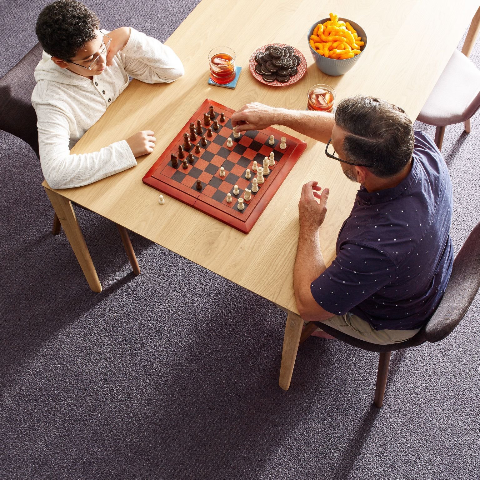 father and son playing chess while eating snacks in a room with gray carpet from Richardson’s Carpet Service in the Williamsburg, VA area